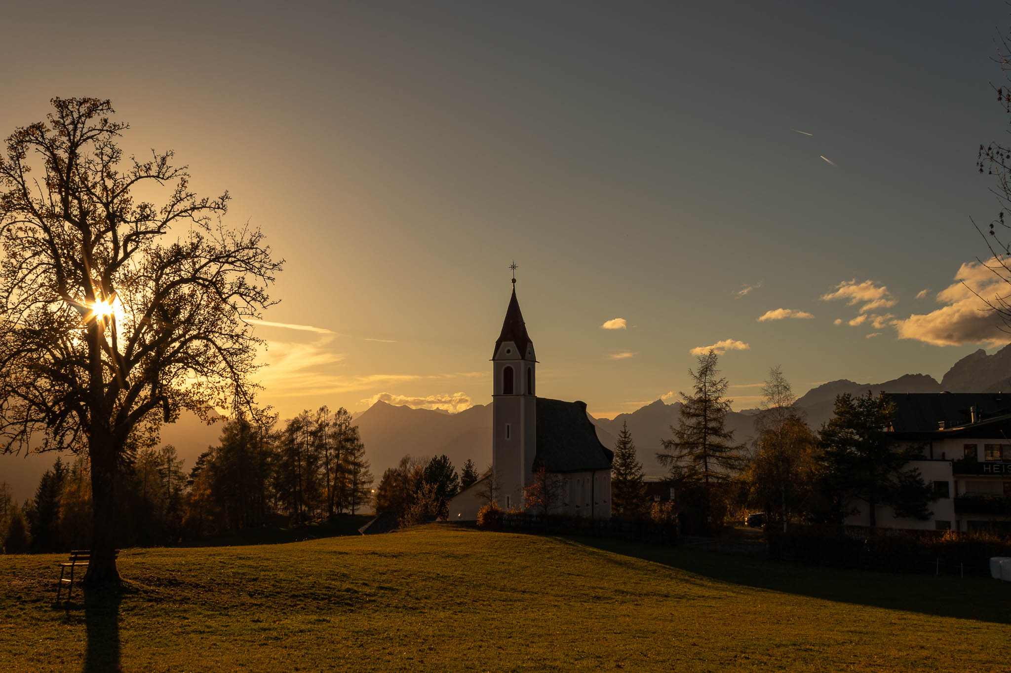 Moesern Church before sunset showing mainly the silouette of the tree and the church beyond this opend field brings nature and the structures that were built by humans so much closer together and reminds me how valuable it is that we put some beauty into our strutures aswell